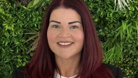 Acquiesce Ltd handout Close up of Danielle Robinson with long brown hair wearing a black blazer and cream top. She is smiling.