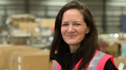 A woman with long dark hair and a pink reflective jacket in a blurred room