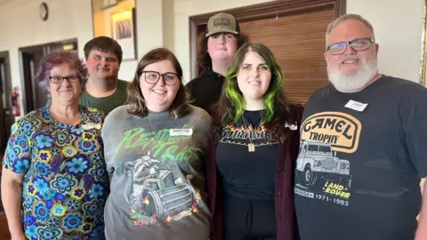 Jimmy Poindexter is standing in a hotel restaurant with his family. He is standing next to his wife and four children.