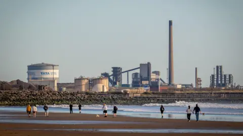 Getty Images People walking along Abaravon Beach with the Tata Steelworks in the background.