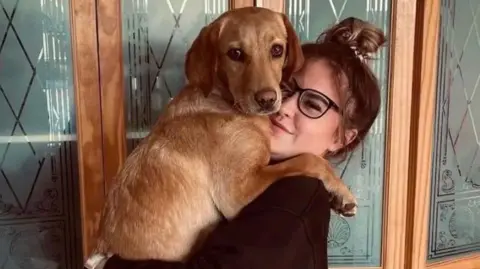 Sussex Police A blonde woman wearing glasses and a black jumper is holding a dog.