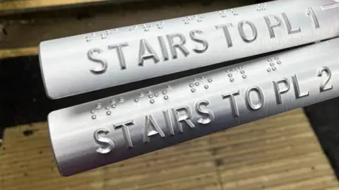 Kit Taylor/BBC Two metal strips showing tactile raised text that says 'stairs to platform 1 and 2'
