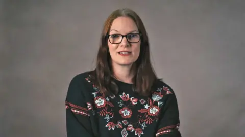 Zara, who wears glasses and a jumper with flowers on it, speaks to the BBC.