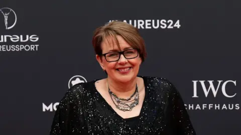 Tanni Grey-Thompson at the 2024 Laureus World Sports Award  in Madrid, she is smiling for the camera and wearing a black dress with sequins, a necklace and black-rimmed glasses