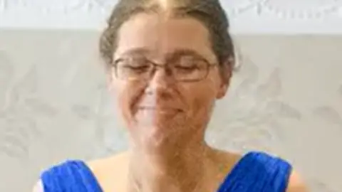 Family photo A close of Steffie Davies wearing a blue dress at her sisters wedding. She wears glasses and her brown hair is tied back. 