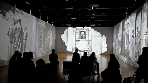 Jewry Wall Museum Museum visitors sit in a darkened room where images are cast onto surrounding walls.