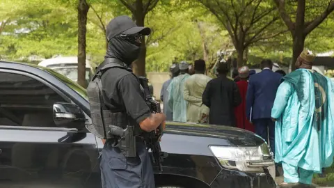 An armed officer in black with shades, cap and facemask stands guard outside the Federal High Court in Abuja on Wednesday 22 April 2026.
