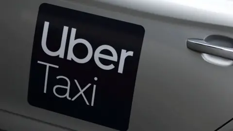A close up picture of an Uber Taxi logo on a silver car. 