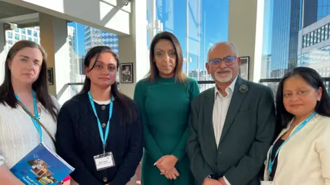 A group of retailers look at the camera. On the left is a woman holding a brochure from a retail conference they are all attending