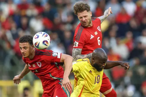 PA Media Wales footballers Joe Rodon and Ethan Ampadu are either side of Belgium's Romelu Lukaka as they challenge for the ball. Rodon has leapt in the air to head the ball and has his eyes closed while leaning on the back of Lukaku