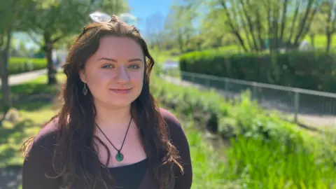 Rhianna Cowdy, Warminster Town Development Officer smiles at the camera while standing next to a footpath and a river.