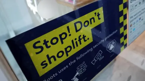 A blue and yellow sign on a window that reads "Stop! Don't shoplift."