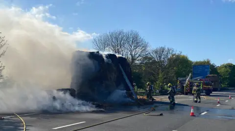 A lorry carrying bales of hay is on fire as fire crews respond on an empty motorway