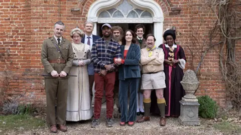 Cast photo of the characters from the show outside Button House, in costume