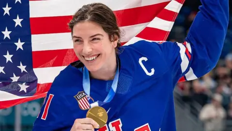 Hilary Knight smiles while holding her gold medal after the USA win women's ice hockey gold at the 2026 Winter Olympics