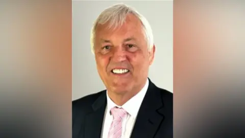Jan Matecki smiles at the camera in an official council portrait. He wars a dark suit, pink tie and white shirt.