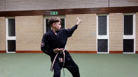 Seb in a black karate costume in a karate pose