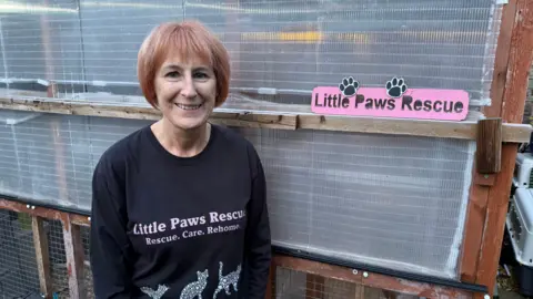 Tracey Bryant wearing a Little Paws Rescue T-shirt and standing next to a small pink sign that says "Little Paws Rescue".