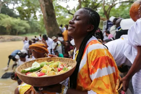 AKINTUNDE AKINLEYE / REUTERS A worshipper of Osun prays with an offering in a calabash at bank of the Osun River during the Osun annual festival at the Osun-Osogbo Sacred Grove in Osogbo, southwest Nigeria, August 9, 2024.