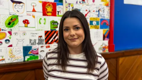 Bethany Carr with brown hair in a striped top standing in front of a wall with hand-drawn images.