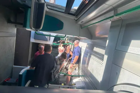 Rachel Heath A train carriage on its side with people standing on the walls of the train.