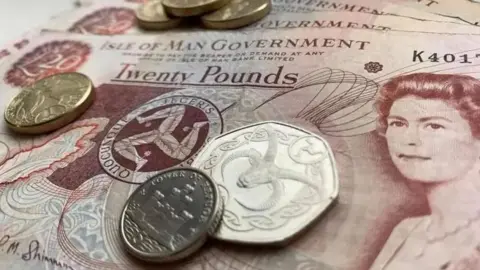 BBC Red and beige £20 notes on a table with four gold round £1 and silver 50p and 10p coins on top of them.