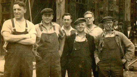 Supplied A sepia archive picture showing six former shipyard workers standing side-by-side, looking at the camera. They are wearing work overalls. 