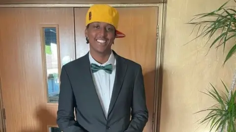 Family Handout Mr Kinuthia dressed in a suit jacket, green bow tie and yellow baseball cap