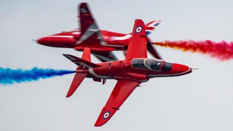 Two Red Arrow jets flying past each other.