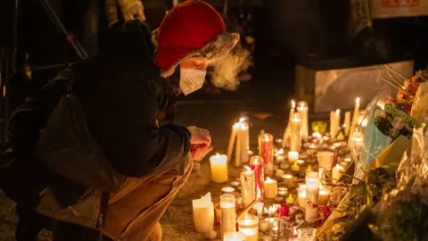 A woman at a vigil in Minneapolis kneeling and looking at candles and flowers following the fatal shooting of a man by immigration agents