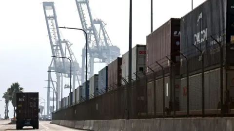 Getty -afbeeldingen Een vrachtwagen drijft langs verzendcontainers die op treinwagons in de haven van Long Beach zijn gestapeld op 4 december 2024 in Long Beach, Californië. 