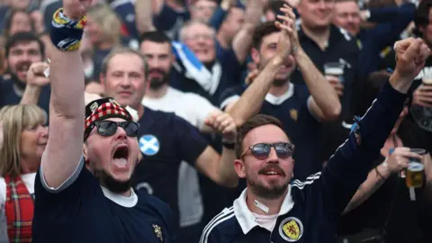 A crowd of Scotland fans, clapping and cheering. 