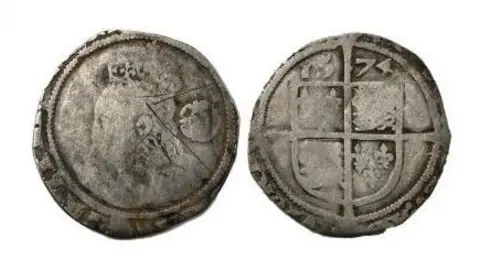 The front and back of the Elizabeth I threepence. The silver coins have lost their circular shape and the edges are worn. The markings on the both faces are worn down. The left image shows a faded portrait of Queen Elizabeth. The right images shows a faded coat of arms in a shield shape and sectioned into quarters, with the date 1574 above it.