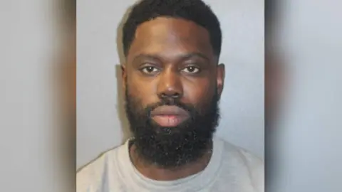 Met Police Justin Clarke-Samuel's police mugshot. He wears a grey top and is looking at the camera.