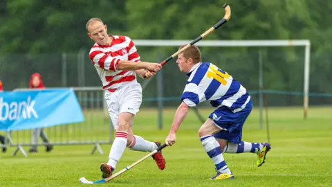 Neil Paterson Lachlan, left, is running while striking a ball. An opposition player tries to put in a tackle.