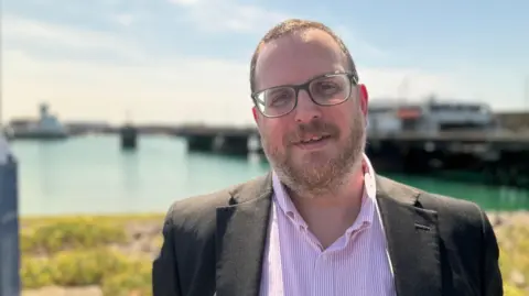 Chris Parker pictured wearing a pink shirt and a black blazer 