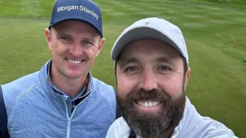 Rick Shiels Rick Shiels has a dark beard and wears a pale blue baseball cap. He is standing on a golf course with Justin Rose, who wears a light blue jacket and navy blue cap. Both men are smiling in a selfie taken by Shiels.