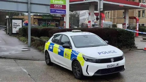 Essex Police An Essex Police car. It is white with police written in blue letters on its bonnet and a blue and yellow stripe on its side with Essex Police on its door. It is parked at an entrance/exit to an Esso  petrol station in Harlow.