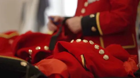 A close up image of one of the Chelsea Pensioners jackets which is red with gold buttons, black cuffs and gold trim