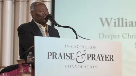 Global Crusade with Kumuyi/Kevin Smart Media William Kumuyi standing at a pulpit behind a sign that says "Inauguration Praise and Prayer Convocation".