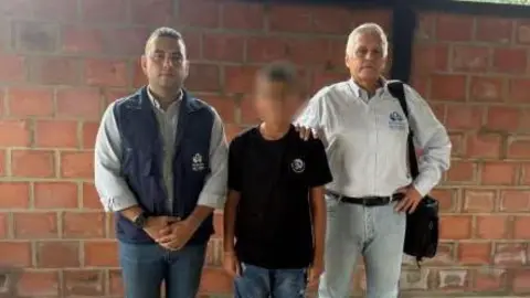 Ombudsman's Office A photo of the Ombudsman's office shows the released boy in a black T-shirt and jeans, flanked by two men from the negotiating team. One man has placed his hand on the boy's shoulder.