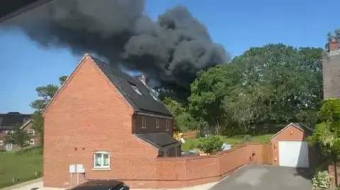 Dark smoke seen rising over a large red brick home.
