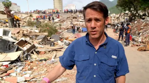 Man in blue shirt walking among rubble after earthquake