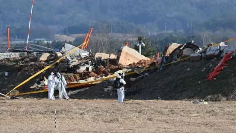 Workers in white protective suits at the scene of the Jeju Air plane crash