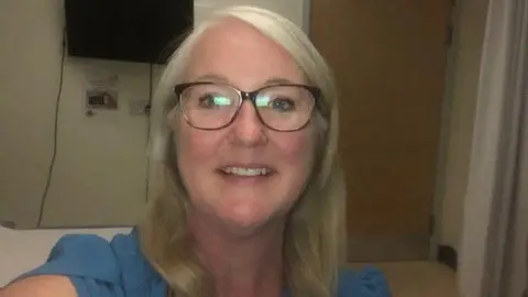 Jane Perry A woman wearing a blue dress and glasses looking to the camera