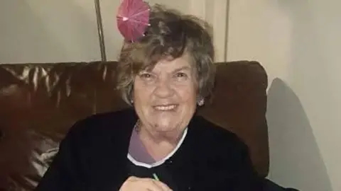 Katherine James A family photo of Nina Morris, an elderly lady, sitting on a sofa, wearing a Christmas party hat and smiling at the camera
