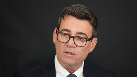 AFP via Getty Images UK PM Andy Burnham wearing a black suit and glasses