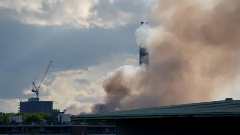 A view from Masthouse Terrace boat stop, on the Isle of Dogs as smoke rises into the sky from a fire at the Landmann Way Reuse and Recycling Centre in Bermondsey, south London