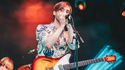 Isaac Neilson performing on stage with a guitar and microphone at Y Not festival in Pikehall in Derbyshire