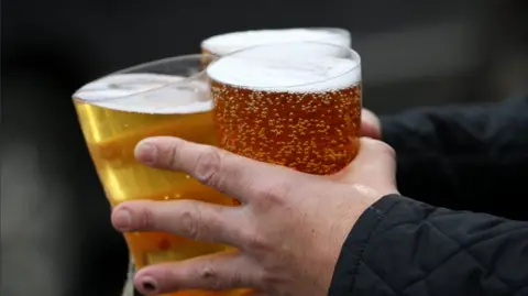 Close-up photograph of a man's hands carrying three pints of beer.